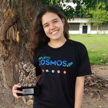 Carlla Vicna sorri e faz pose para foto. Ela segura um troféu