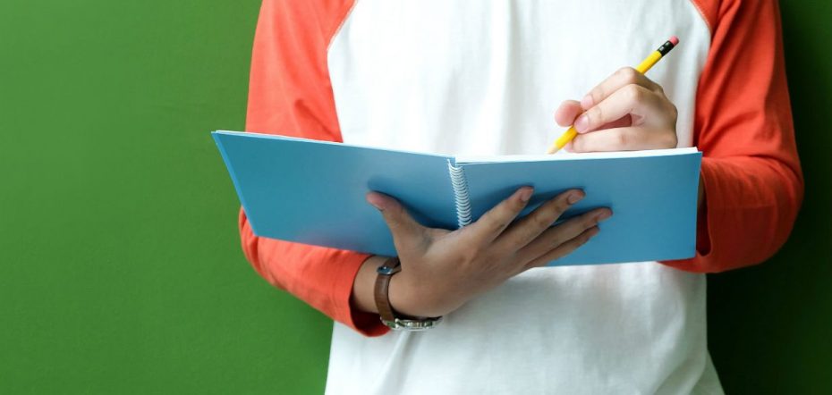 Foto do dorso de uma pessoa segurando um caderno e um lápis