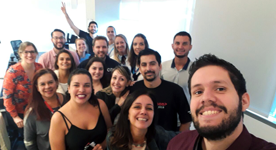 Foto de um grupo de pessoas posando para uma selfie. Há homens e mulheres e eles sorriem enquanto a foto é tirada.