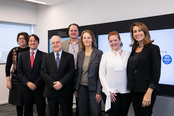 Foto de sete pessoas, sendo três homens e sete mulheres, lado a lado e sorrindo, em uma sala de escritório. Ao fundo, há uma tela com o logo do Instituto Claro.