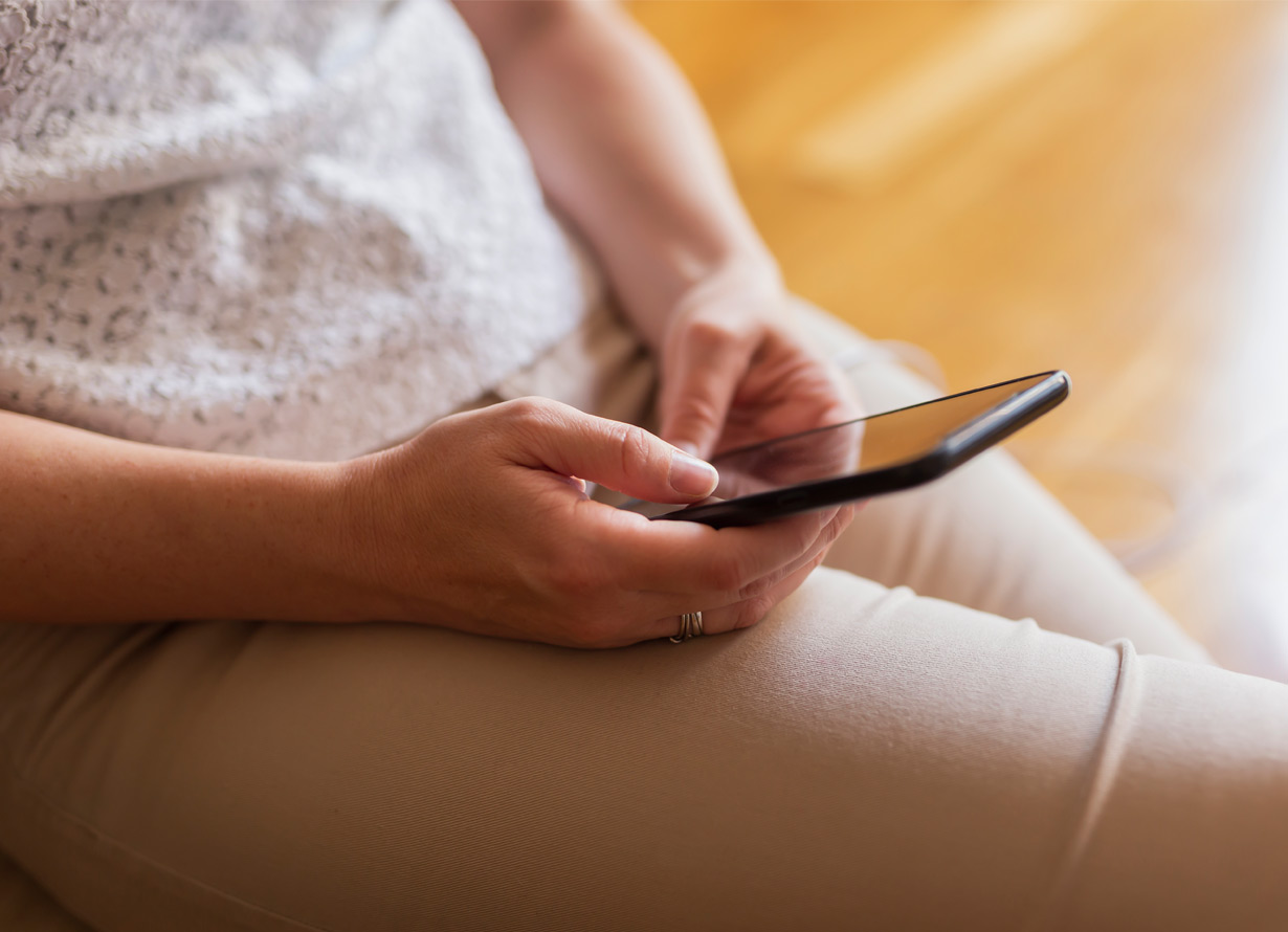 Foto, em detalhe, de mãos femininas segurando um celular.