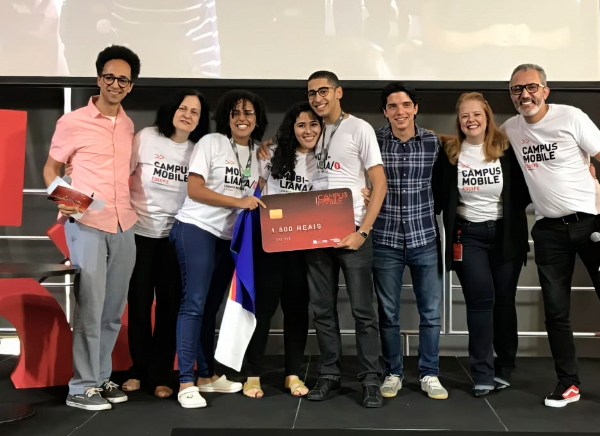 Foto de um grupo diverso de pessoas lado a lado sobre um palco. Elas se abraçam e sorriem