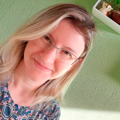 Foto em formato selfie de uma mulher loira. Ela usa óculos de grau e sorri
