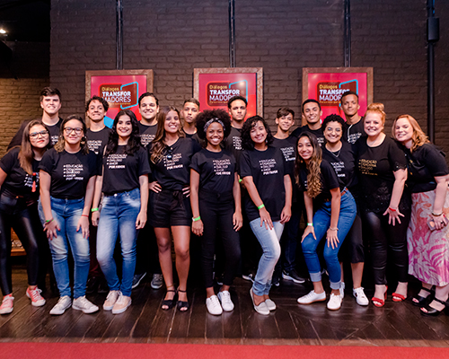 foto de um grupo de jovens em pé posando para uma fotografia. Eles estão sorrindo e vestem camisetas pretas