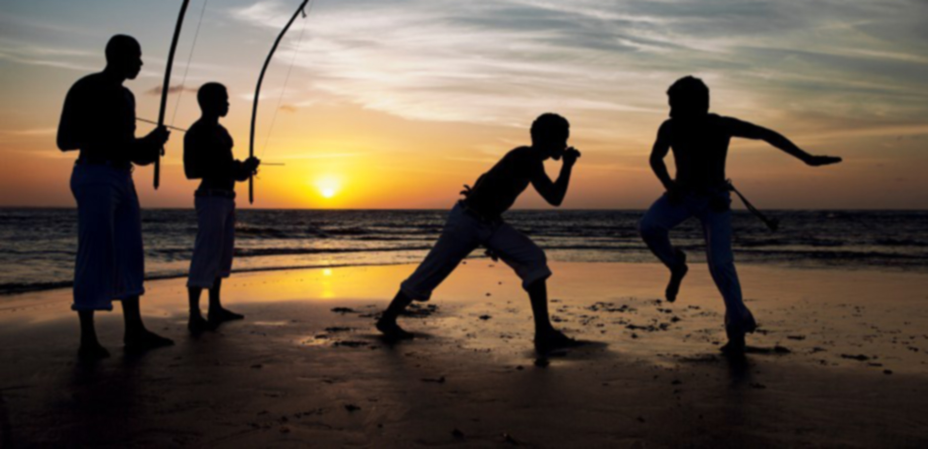 Foto de 2 garotos jogando capoeira na beira do mar ao entardecer